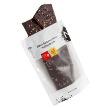 Load image into Gallery viewer, Sesame brittle pouring out of 3oz sized white bag stating “Black Sesame Seed Toffee Brittle” and NeoCocoa logo, with a Good Food Award sticker and a SOFI Gold award sticker.