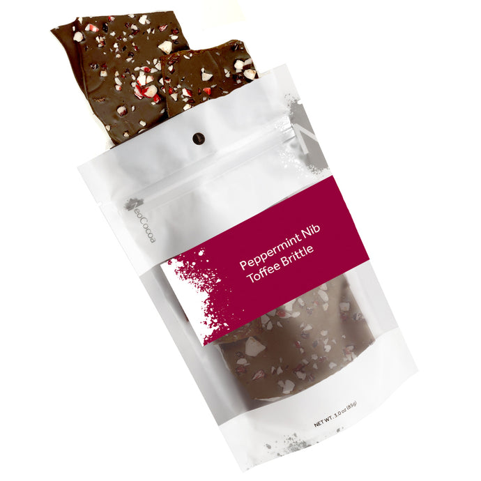 Peppermint nib brittle pouring out of 3oz sized bag with orange label stating “Peppermint Nib Toffee Brittle” and NeoCocoa logo on a white background.
